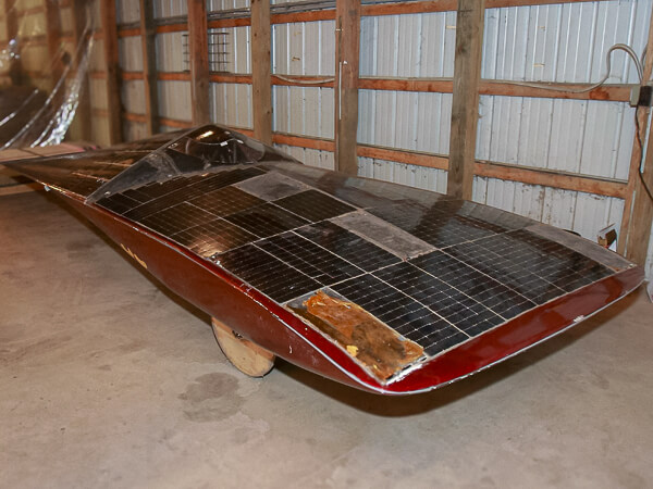 Solar-powered vehicle with a sleek design and solar panel-covered body inside a building.