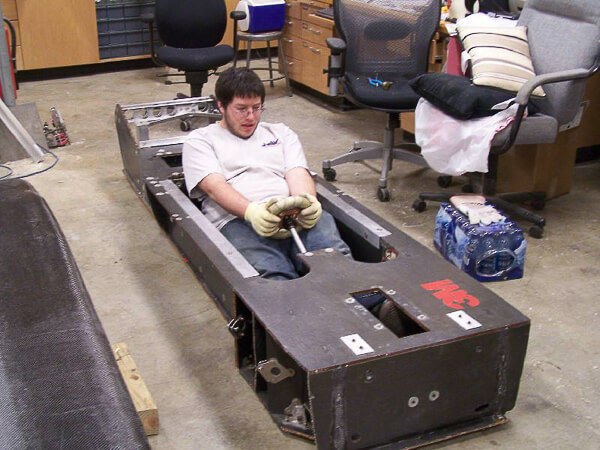 Man sitting in a large metal chassis in a workshop.