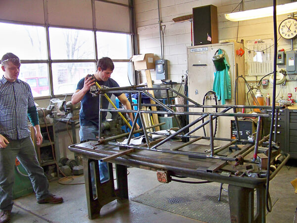 Three people working on a foam and wood structure in a workshop.