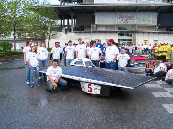 A group of people posing with a solar-powered vehicle covered in solar panels, with the number 5 on the front.