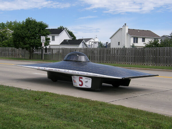 A solar car with number 5 on its side driving on a suburban road.