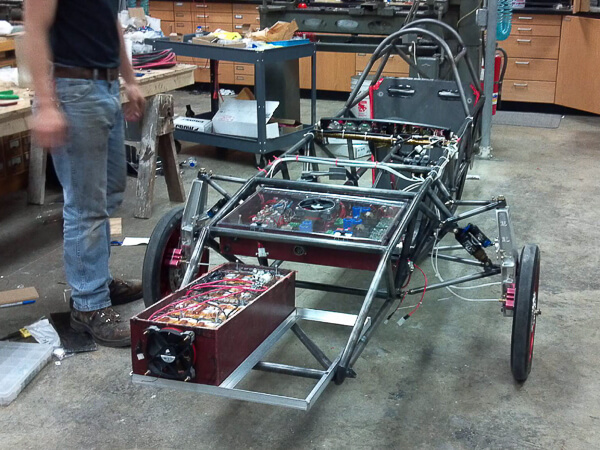 Partially assembled solar car in a workshop with exposed framework and mechanical components.