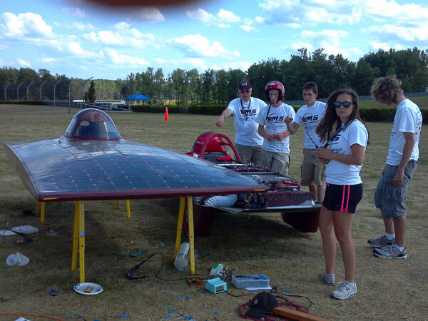 Group of people standing next to a solar-powered vehicle on a grassy field.