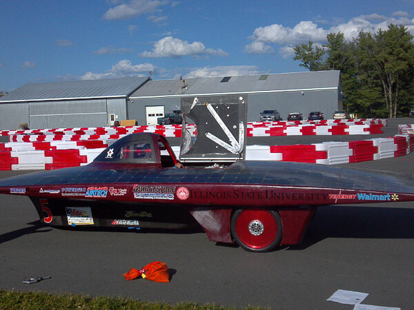 A solar-powered car with "Illinois State University" on the side, near red and white barriers.