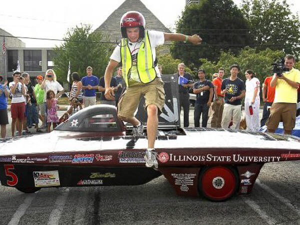 Person stepping out of a solar car with "Illinois State University" on the side, surrounded by spectators.