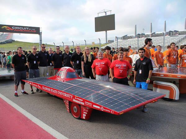 Group with a red solar car labeled "Illinois State University" at a race track.
