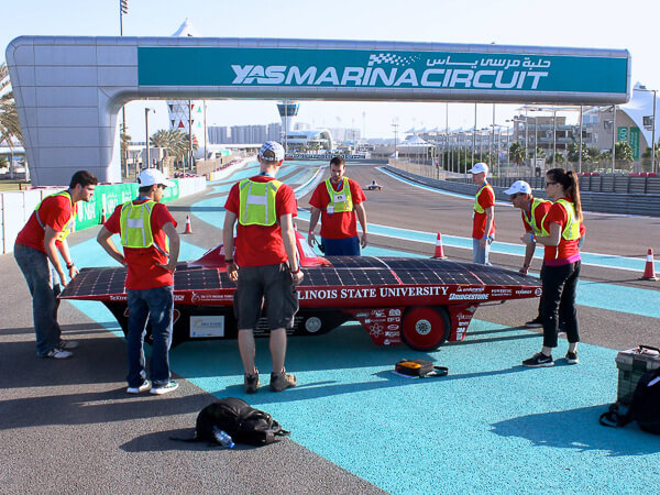 A team gathers around a solar-powered car on a race track at Yas Marina Circuit.