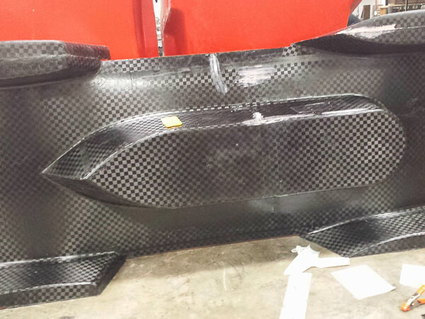 Close-up of a carbon fiber car underbody with checkered pattern and aerodynamic features.