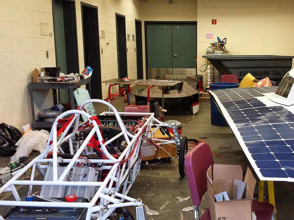 A cluttered workshop with a white vehicle frame, solar panel, and scattered tools.