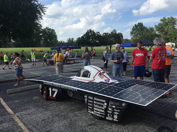 Solar-powered car with Illinois State University branding and solar panels displayed outdoors with people in the background.