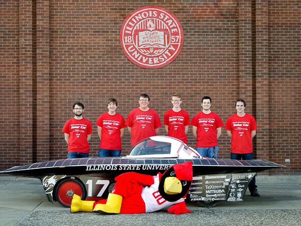 Team posing with a solar car and a redbird mascot in front of an Illinois State University emblem.