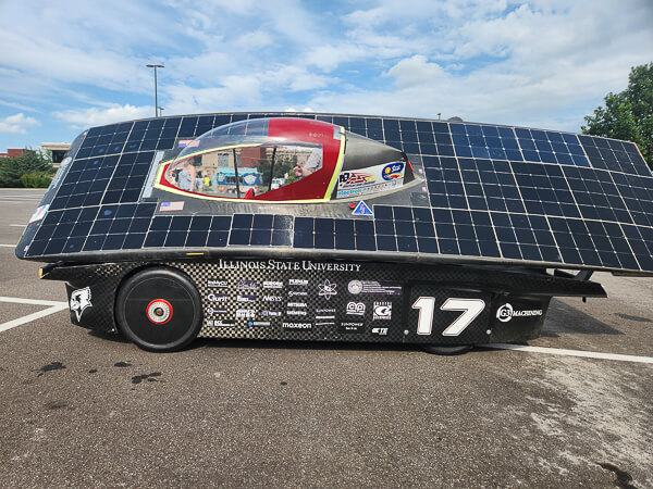 Solar-powered vehicle with solar panels and a transparent cockpit parked outdoors.