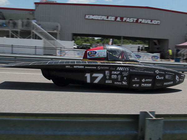 Solar-powered race car number 17 on a racetrack with a building in the background.